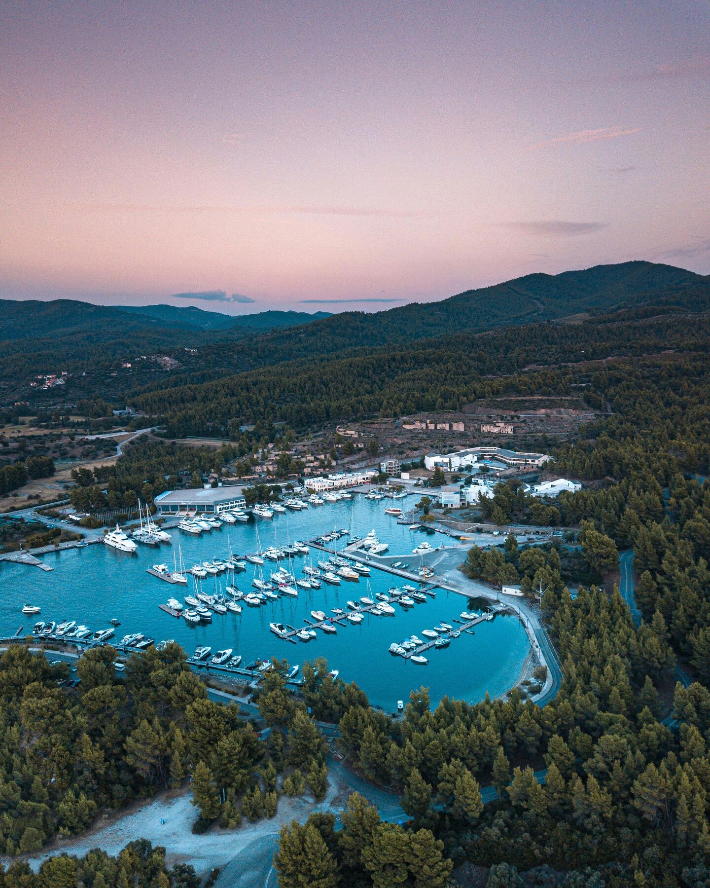 A small marina below forested hills under a soft pink dusk sky